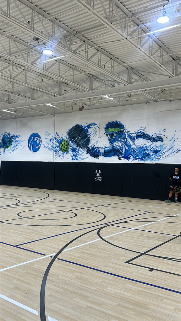 Veio Sports Wall Pads lining a pickleball court under a custom mural